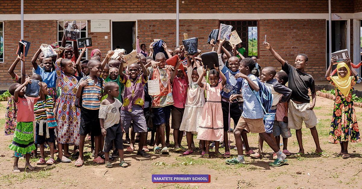 Kinder sitzen in Malawi auf dem Boden umgeben von Maiskolben und blicken in die Kamera
