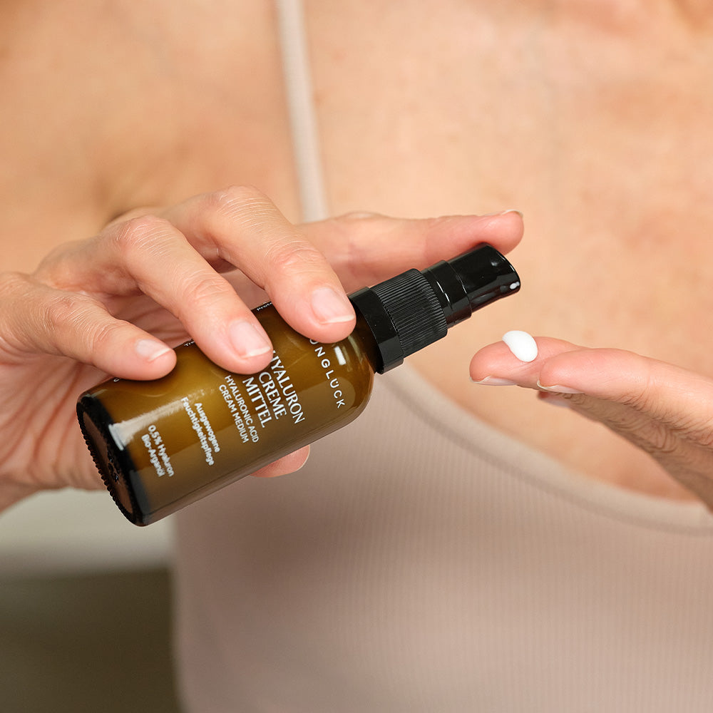 Eine Frau, die ein Braunglasfläschchen mit schwarzer Pipette in der Hand hält und eine weisse Creme auf ihren Finger gibt.