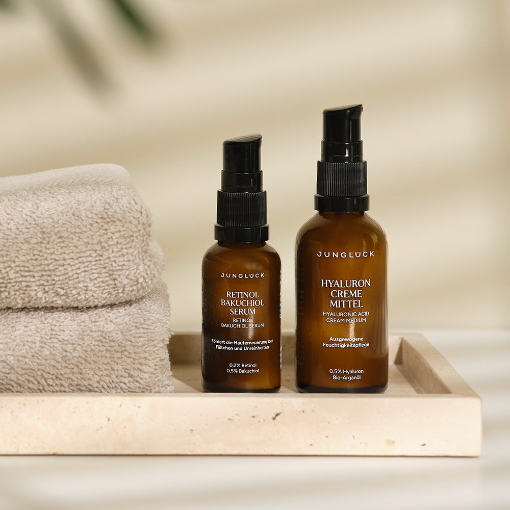 Glatt Gepflegt Set mit zwei Braunglasflaschen: Retinol Bakuchiol Serum und Hyaluron Creme Mittel, auf einem Beistellteller