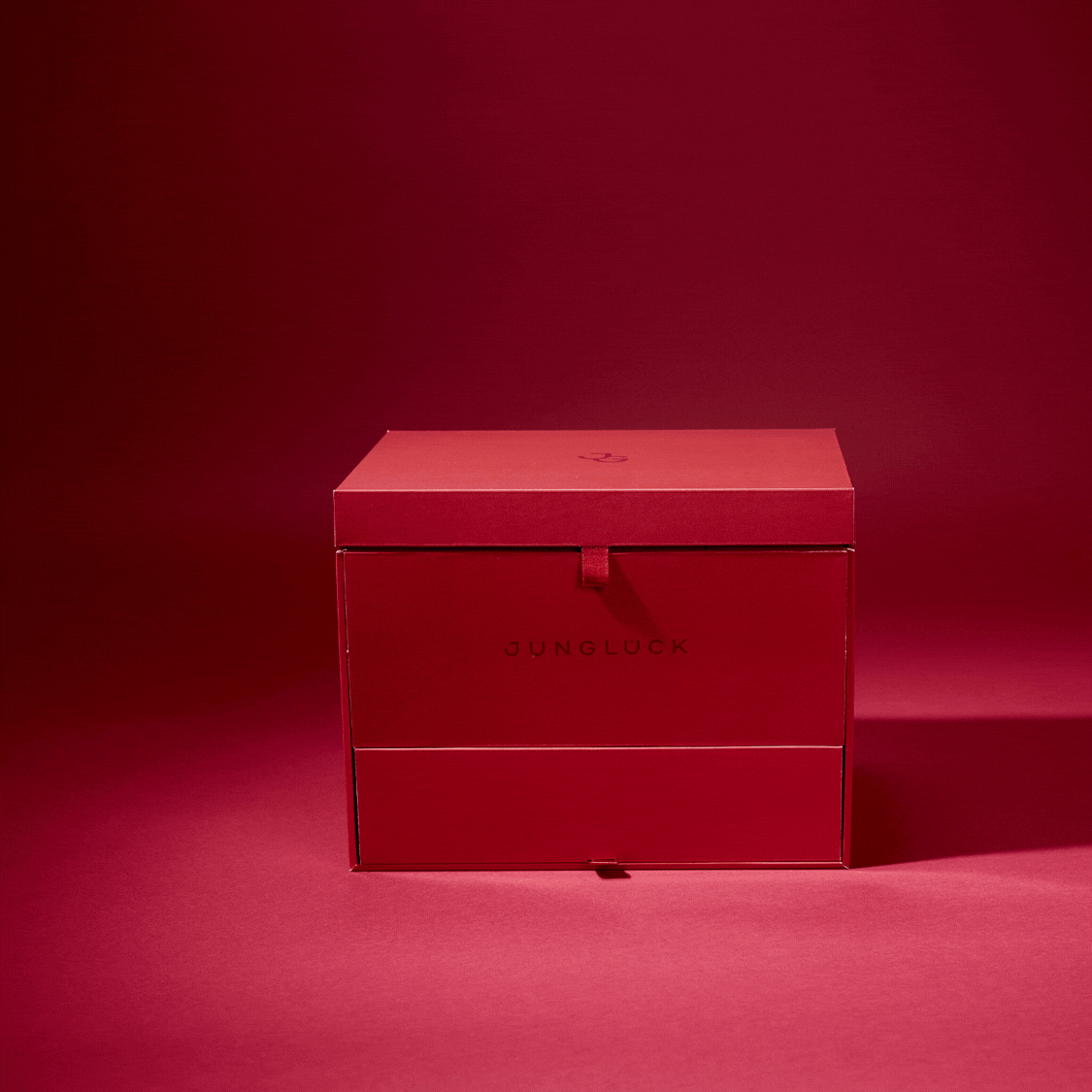 Rote, elegante Box von JUNGLÜCK mit dezenter Beschriftung, auf farbigem Hintergrund.