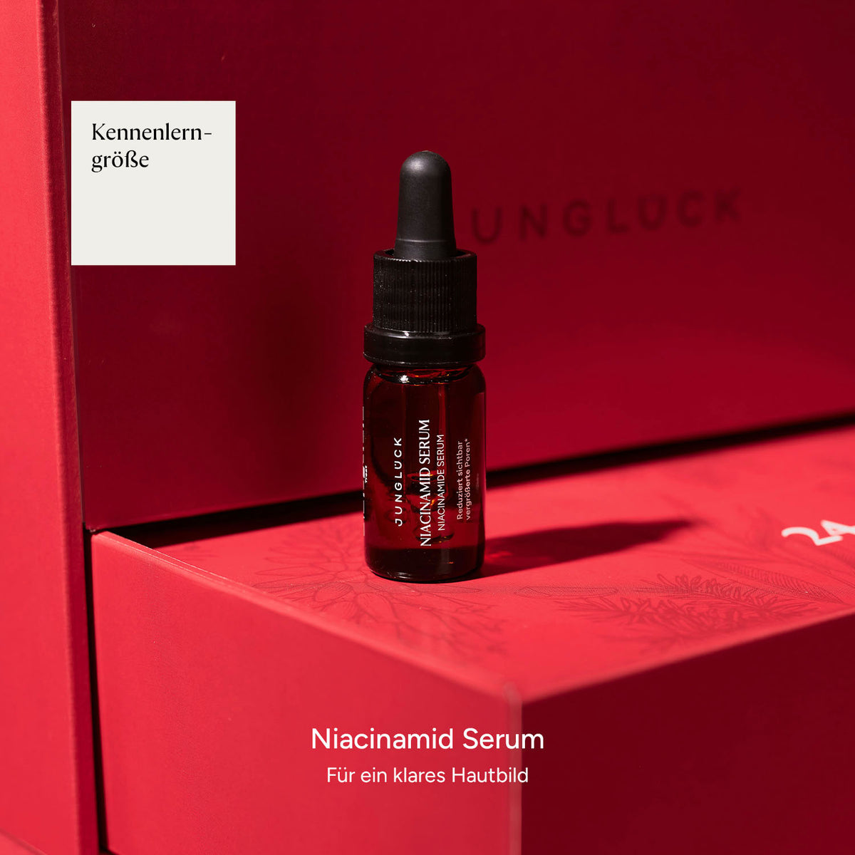 Braunglasflasche mit Niacinamid Serum auf einem roten Hintergrund, textlich umrahmt von 'Kennenlerngrösse' und Produktinfo.