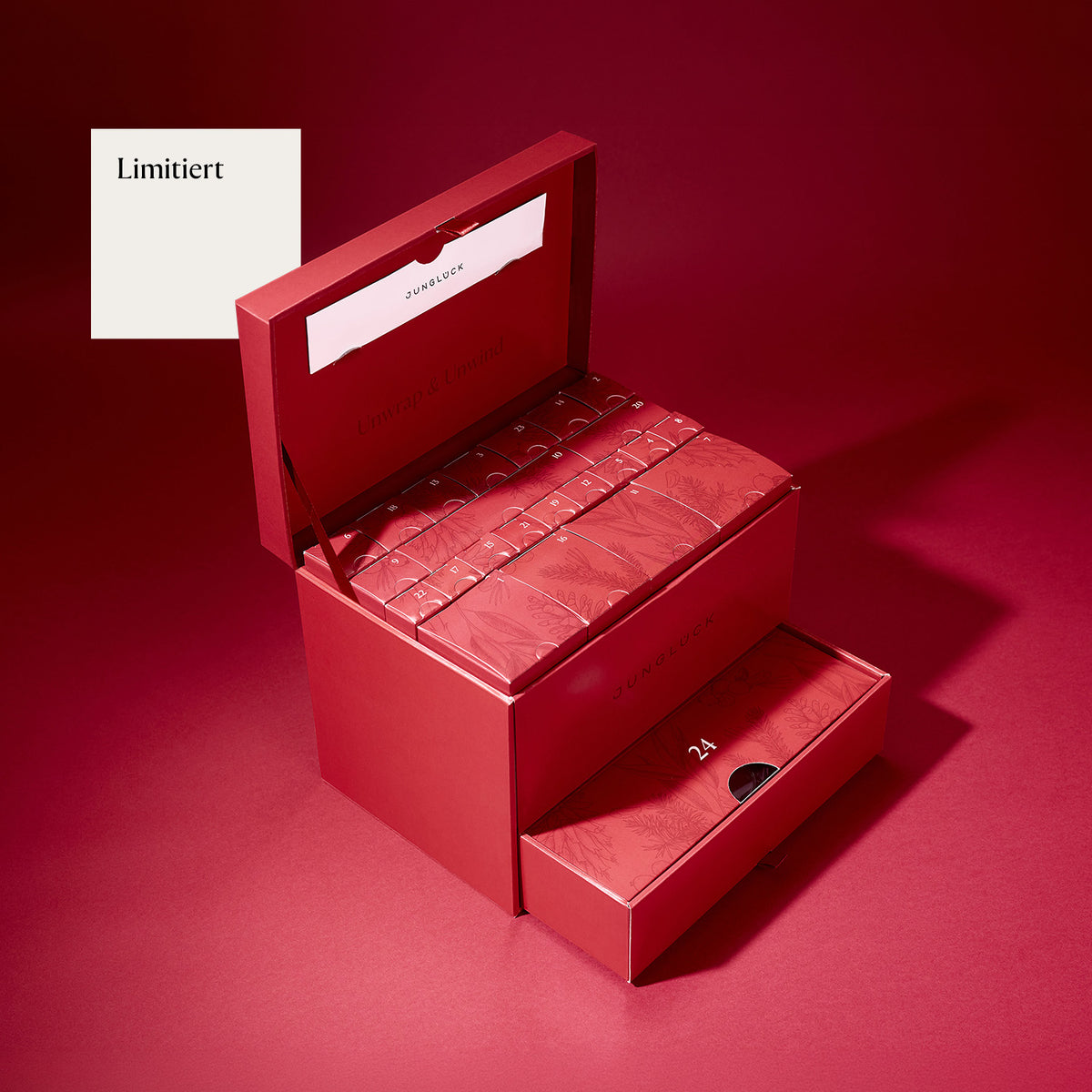 Eine limitierte rote Geschenkbox von JUNGLÜCK, geöffnet mit 24 einzelnen, dekorativen Produkten darin. Im Hintergrund ein