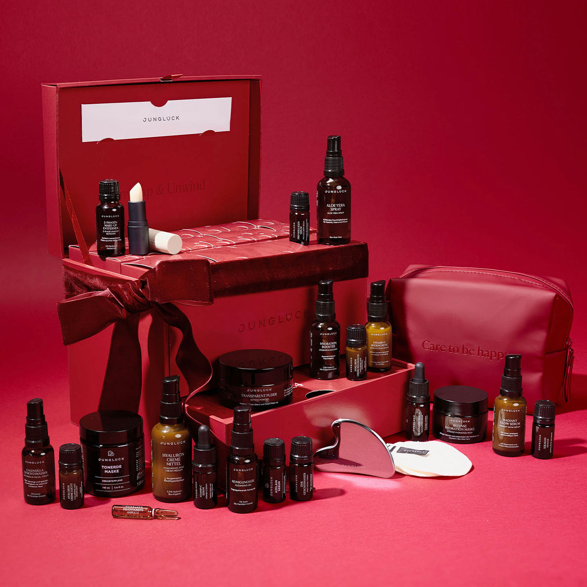 JUNGLÜCK-Produktset in rotem Karton, mehrere Braunglasflaschen, Pflegeprodukte und ein Kosmetiktäschchen.