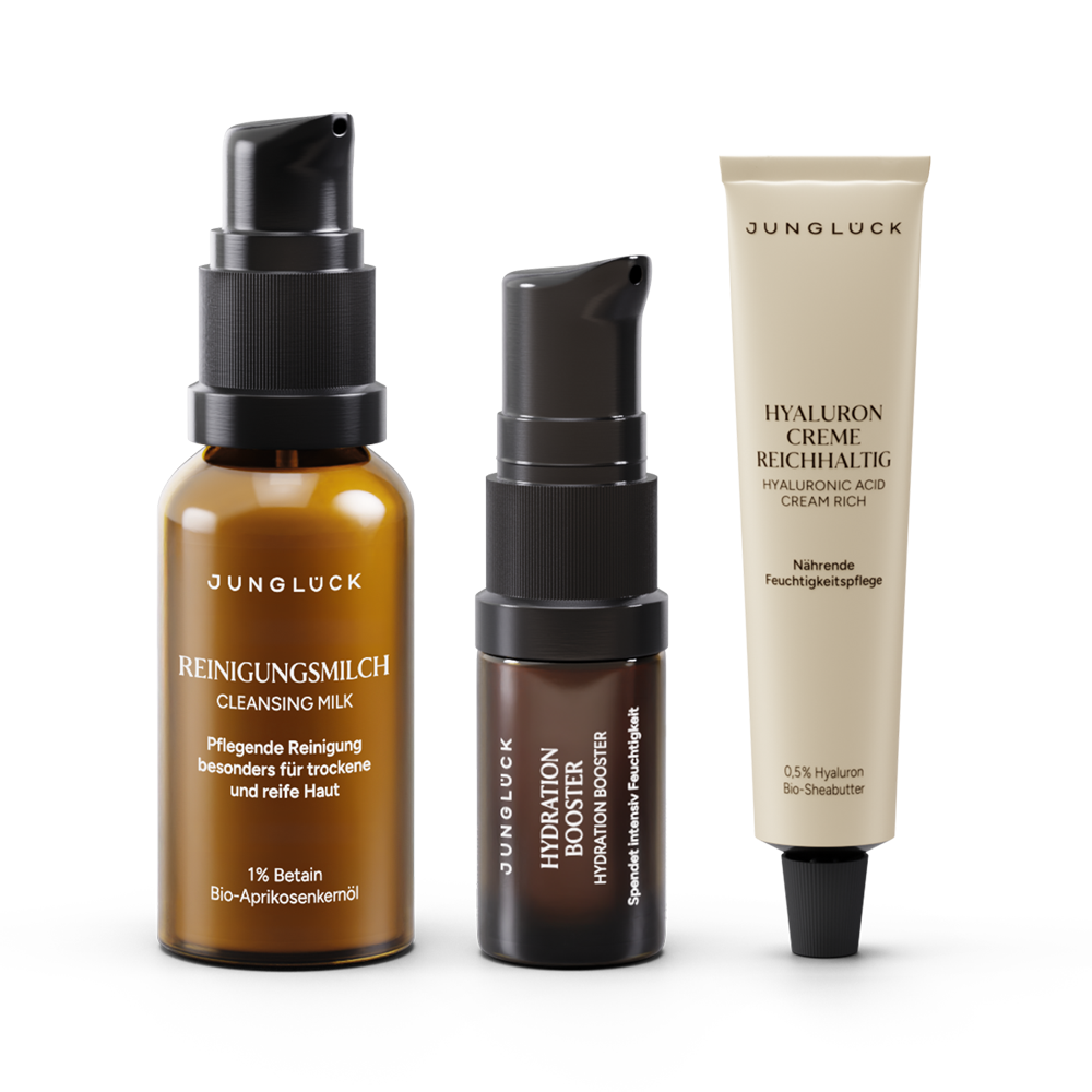 Drei JUNGLÜCK-Produkte: eine braune Flasche mit Reinigungmilch, ein Pumpfläschchen mit Hautserum, und eine Tube mit
